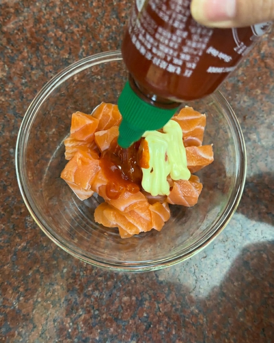Ajout dun filet de mayonnaise crémeuse et de sauce pimentée rouge sur les dés de saumon cru.