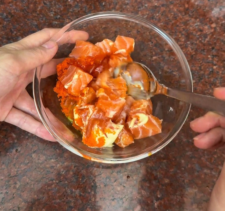 Un bol en verre contenant des dés de saumon frais mélangés à des œufs de poisson et une sauce crémeuse orange.