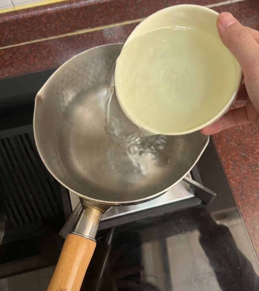 Une main versant de leau claire dun bol en céramique dans une casserole sur une cuisinière.