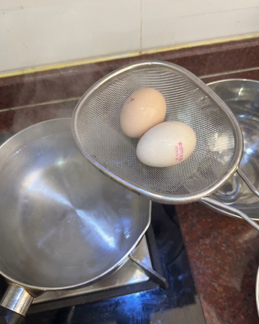 Une écumoire tenant deux œufs cuits au-dessus dune casserole, prête à les plonger dans un bol deau glacée.