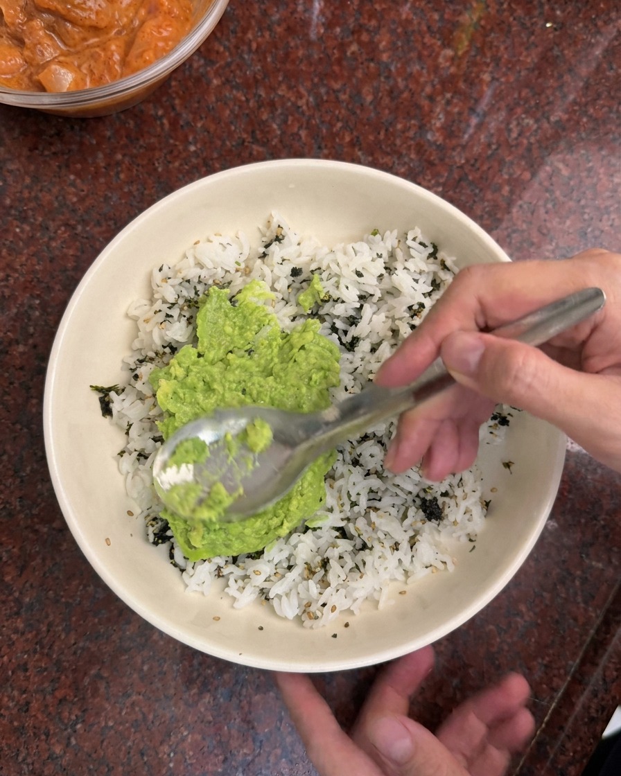 Une cuillère étalant la purée davocat sur un lit de riz blanc et de paillettes dalgues dans un bol blanc.