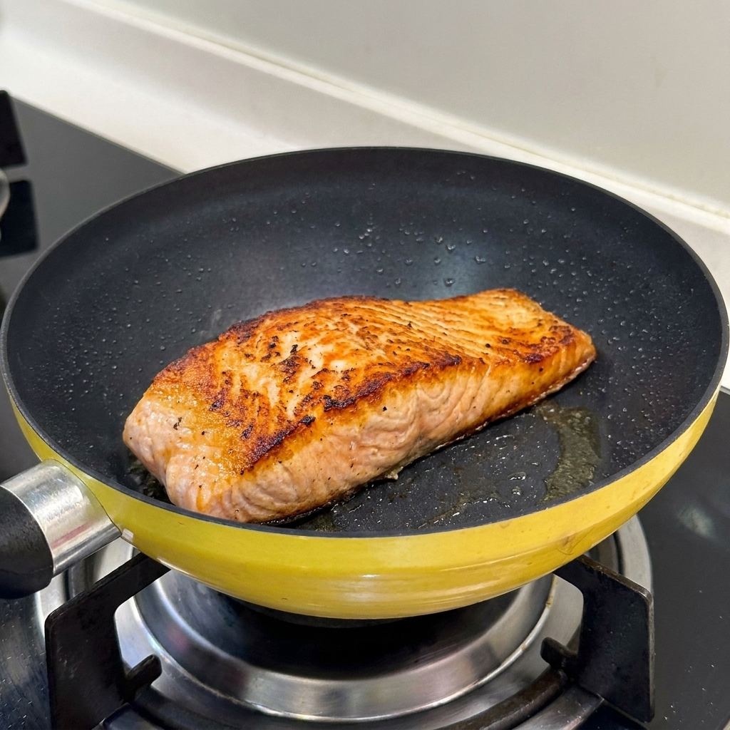 Un filet de saumon saisi dans une poêle jaune montrant une surface parfaitement dorée et croustillante.