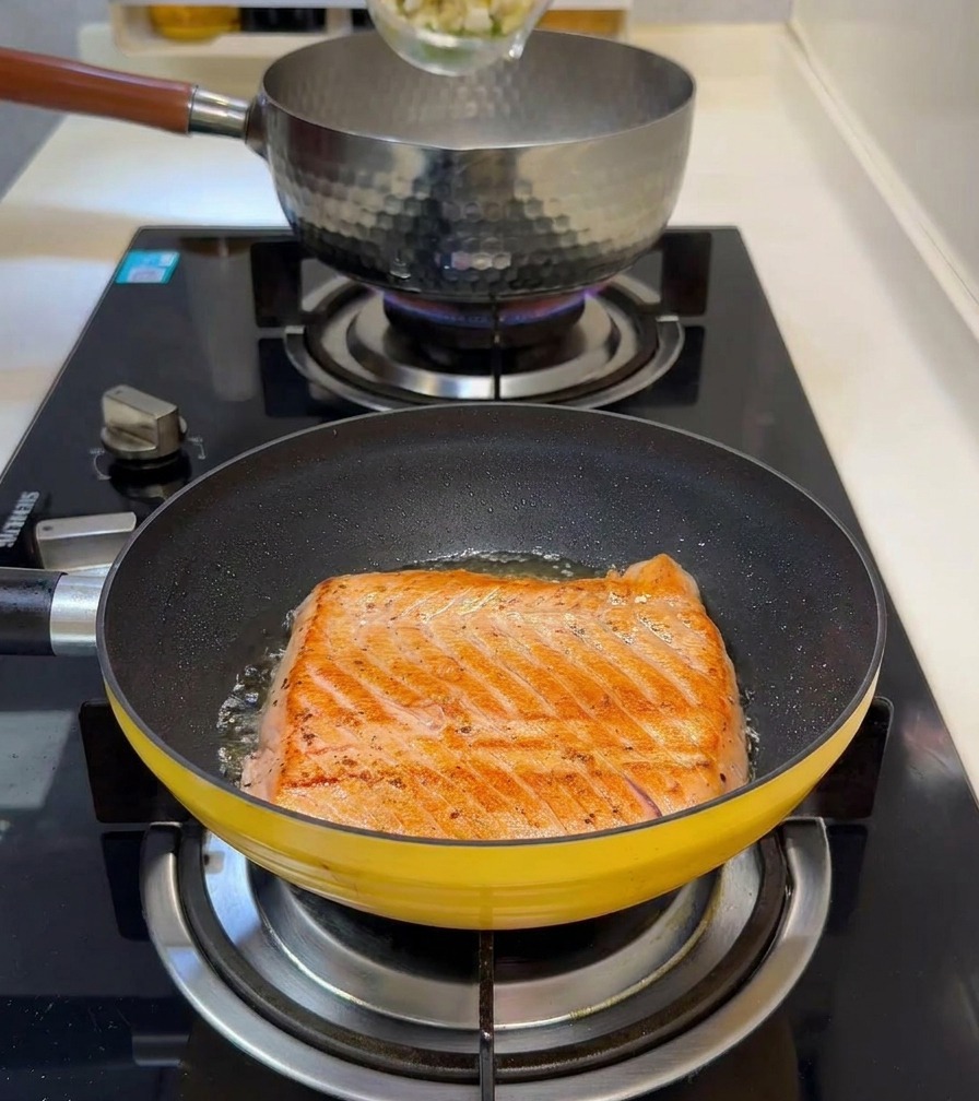 Dés de pousses de bambou et petits pois versés dans une casserole deau bouillante avec un filet de saumon qui saisit au premier plan.
