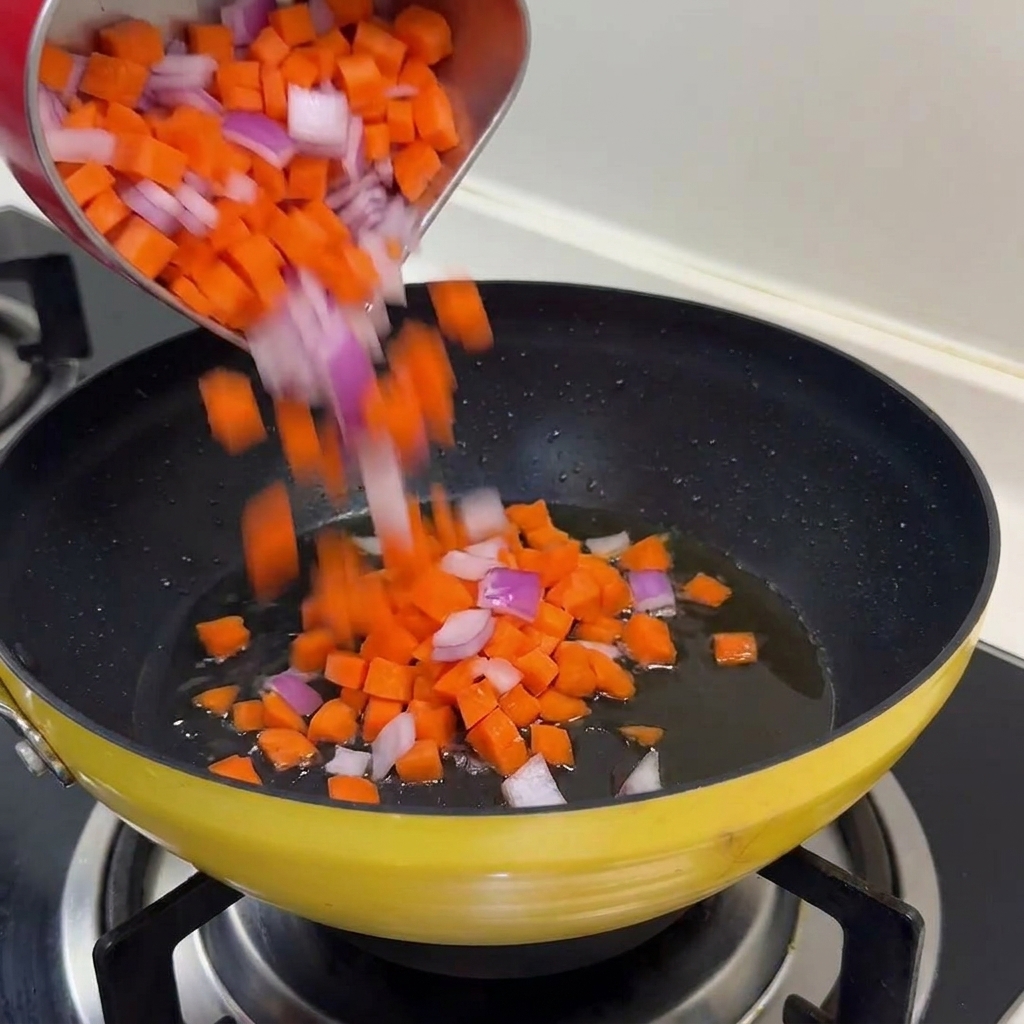 Un mélange de carottes coupées en dés et doignons rouges versé dans une poêle jaune avec de lhuile frémissante.