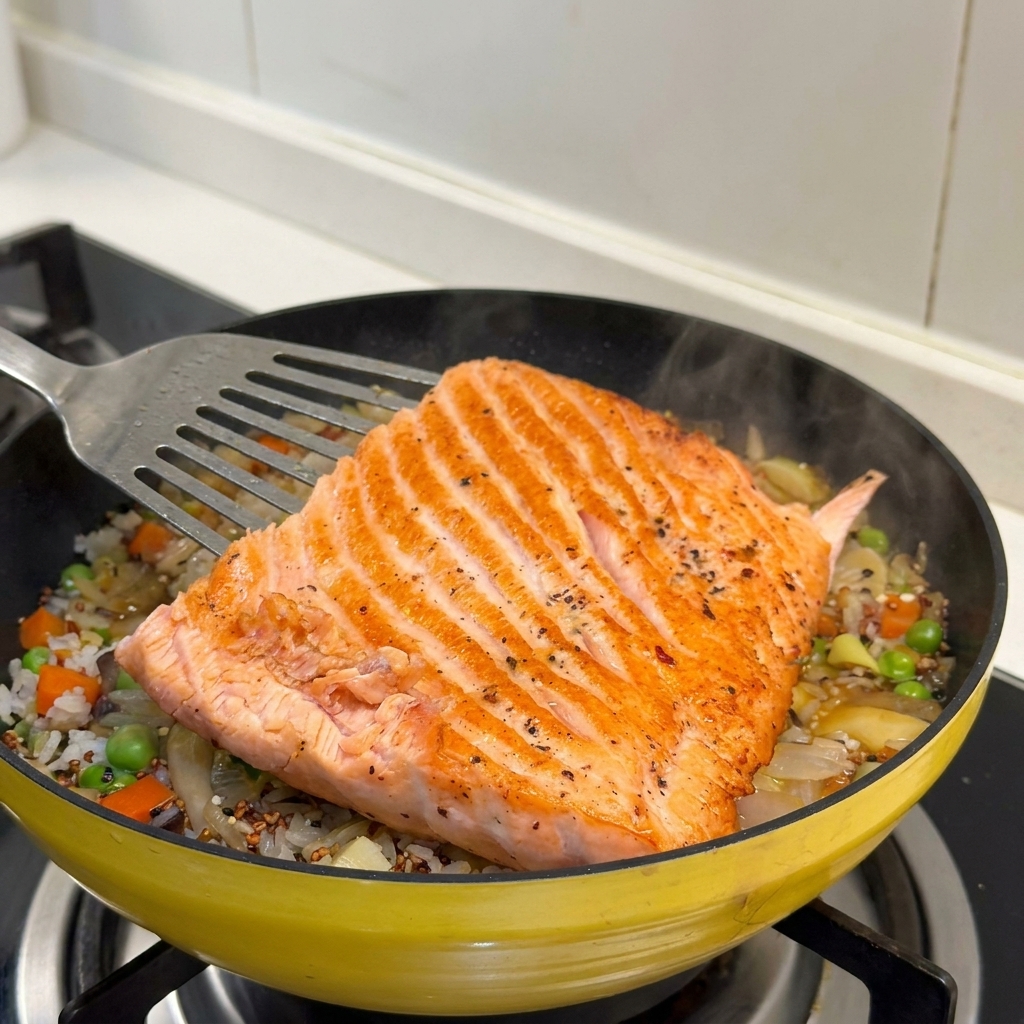 Un large filet de saumon doré posé sur un lit de riz assaisonné et de légumes variés dans une poêle jaune.