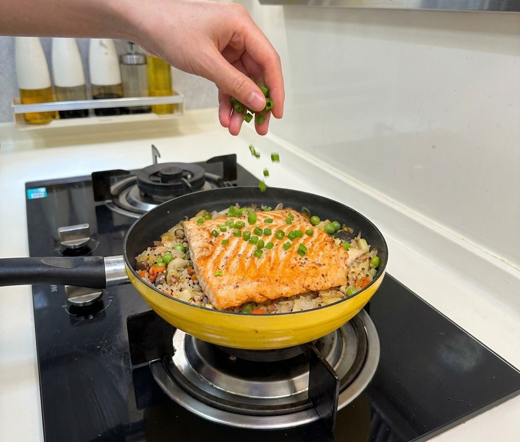 Une main parsemant des oignons verts hachés sur le plat de riz au saumon et légumes terminé.