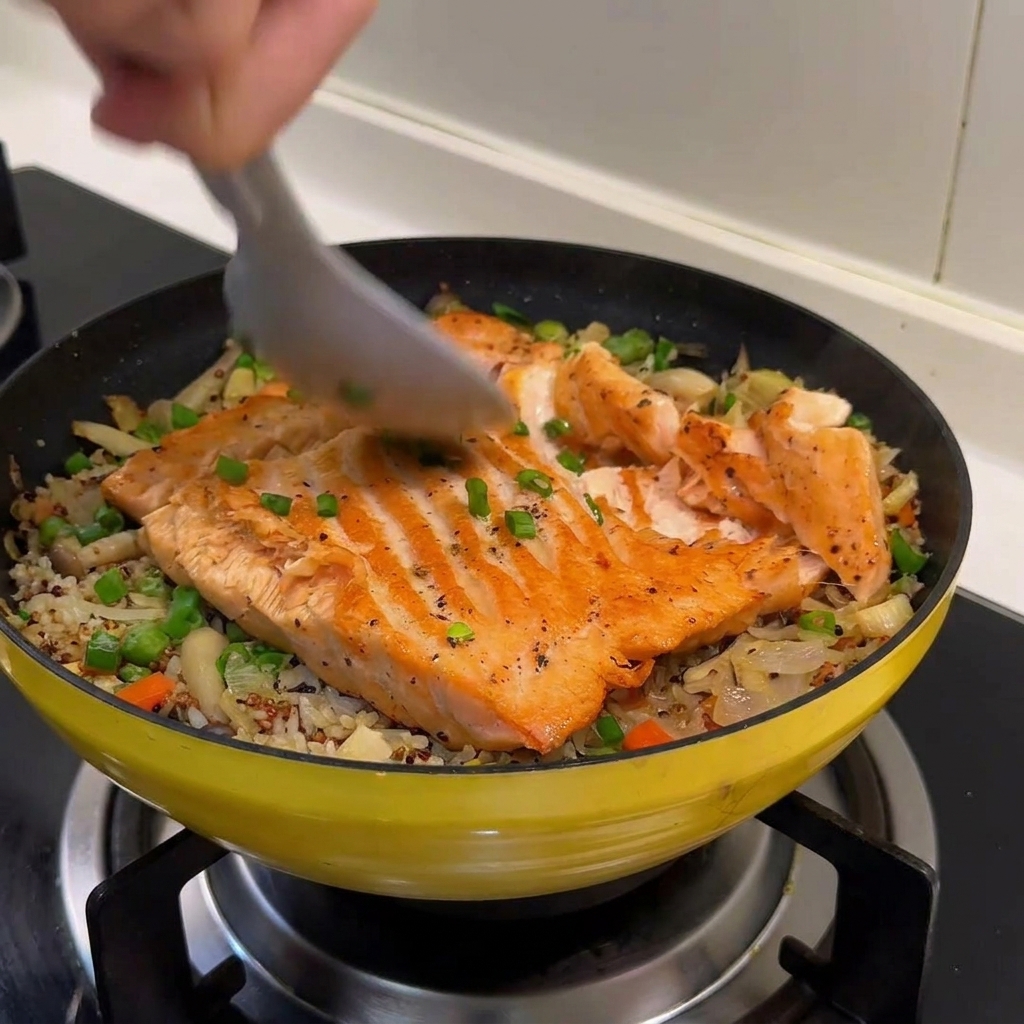 Une cuillère en métal séparant un filet de saumon cuit en lamelles sur un lit de riz braisé et de légumes.