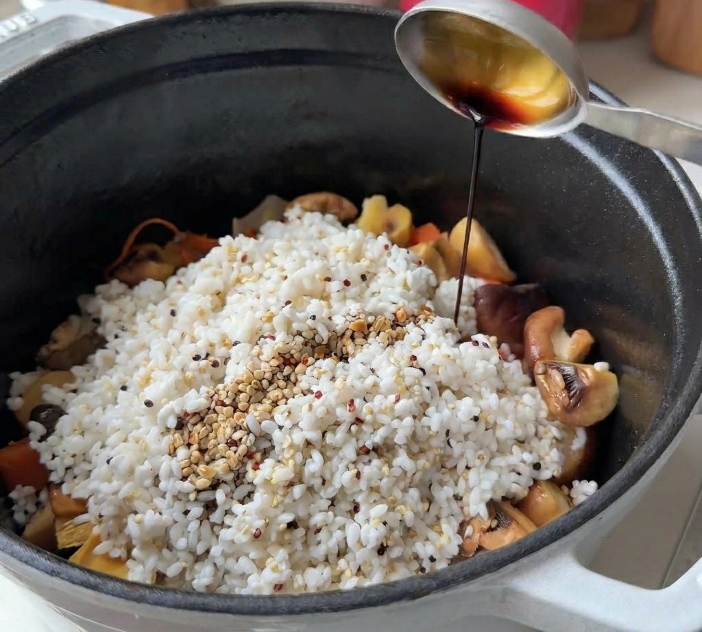 Une cuillère en métal versant de la sauce soja sur le riz, le quinoa et les légumes dans une cocotte noire.