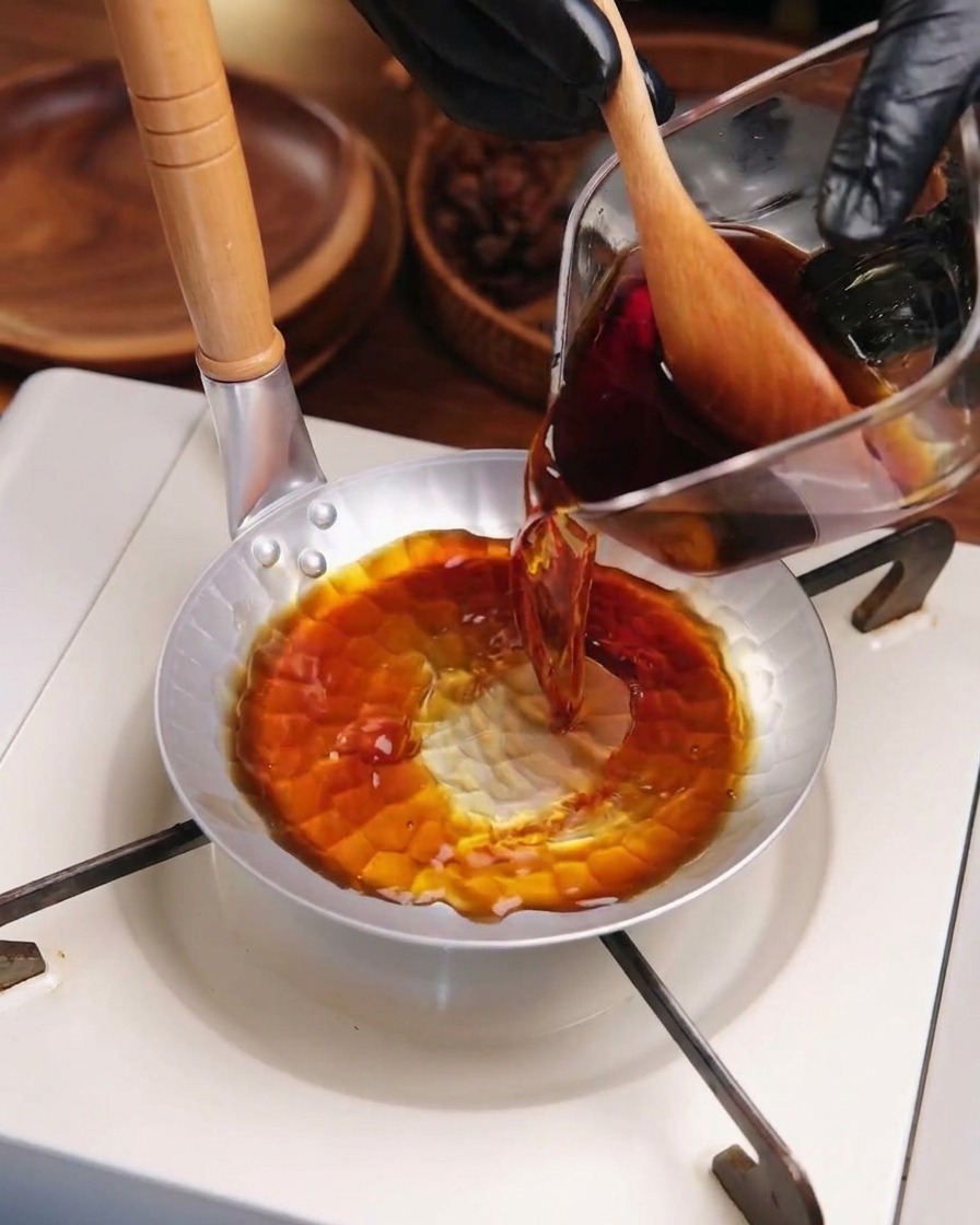 Sauce katsudon sombre versée dun verre doseur dans une petite poêle métallique sur un réchaud portable.