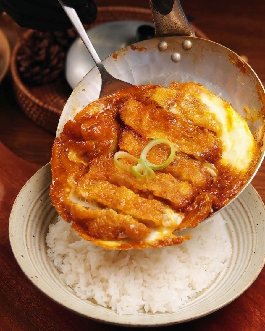 Le mélange porc et œufs cuit glissant dune poêle peu profonde sur un bol de riz blanc bien aéré.