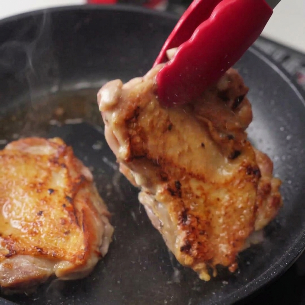 Une pince soulevant un morceau de poulet frit montrant une peau très dorée et croustillante avec de la vapeur.