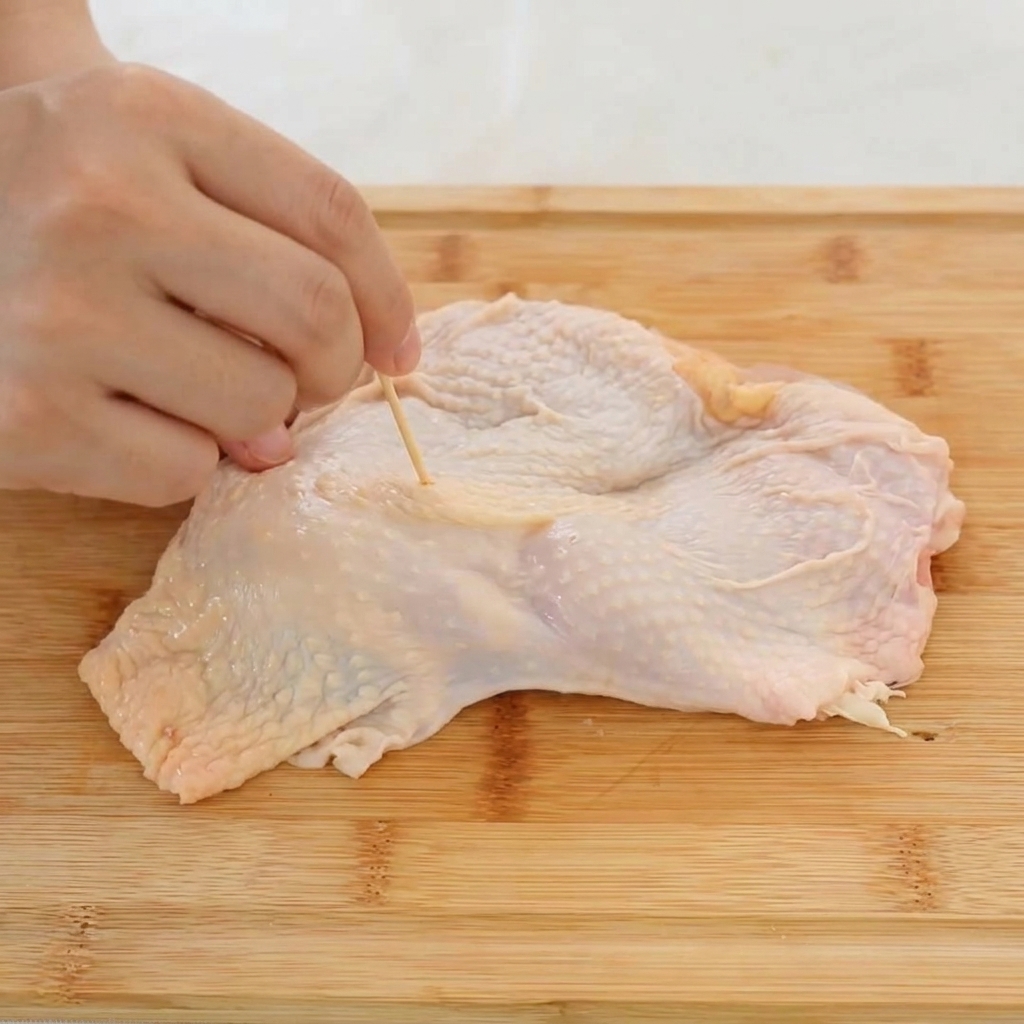 Gros plan sur une main utilisant un cure-dent pour percer des trous dans la peau dune cuisse de poulet.