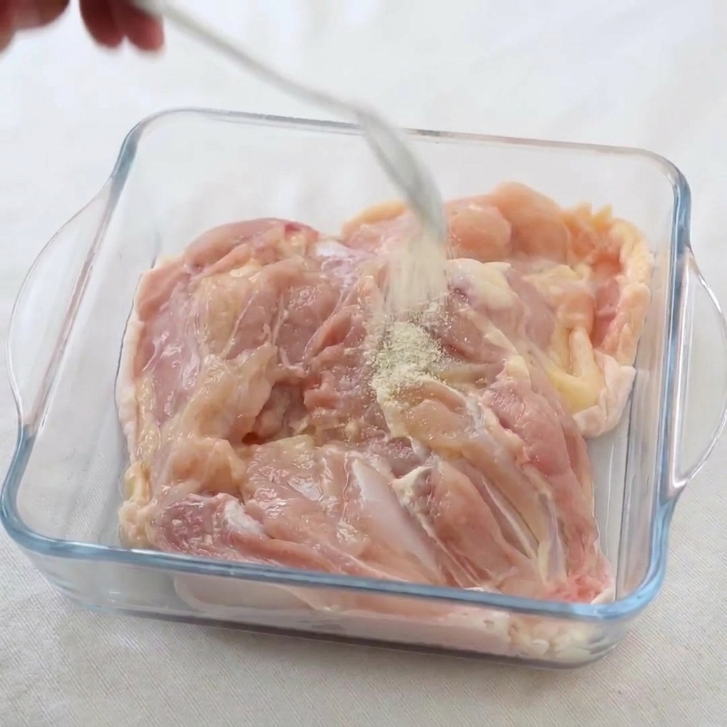 Saupoudrage de poivre blanc et de sel sur les cuisses de poulet crues dans un plat en verre.