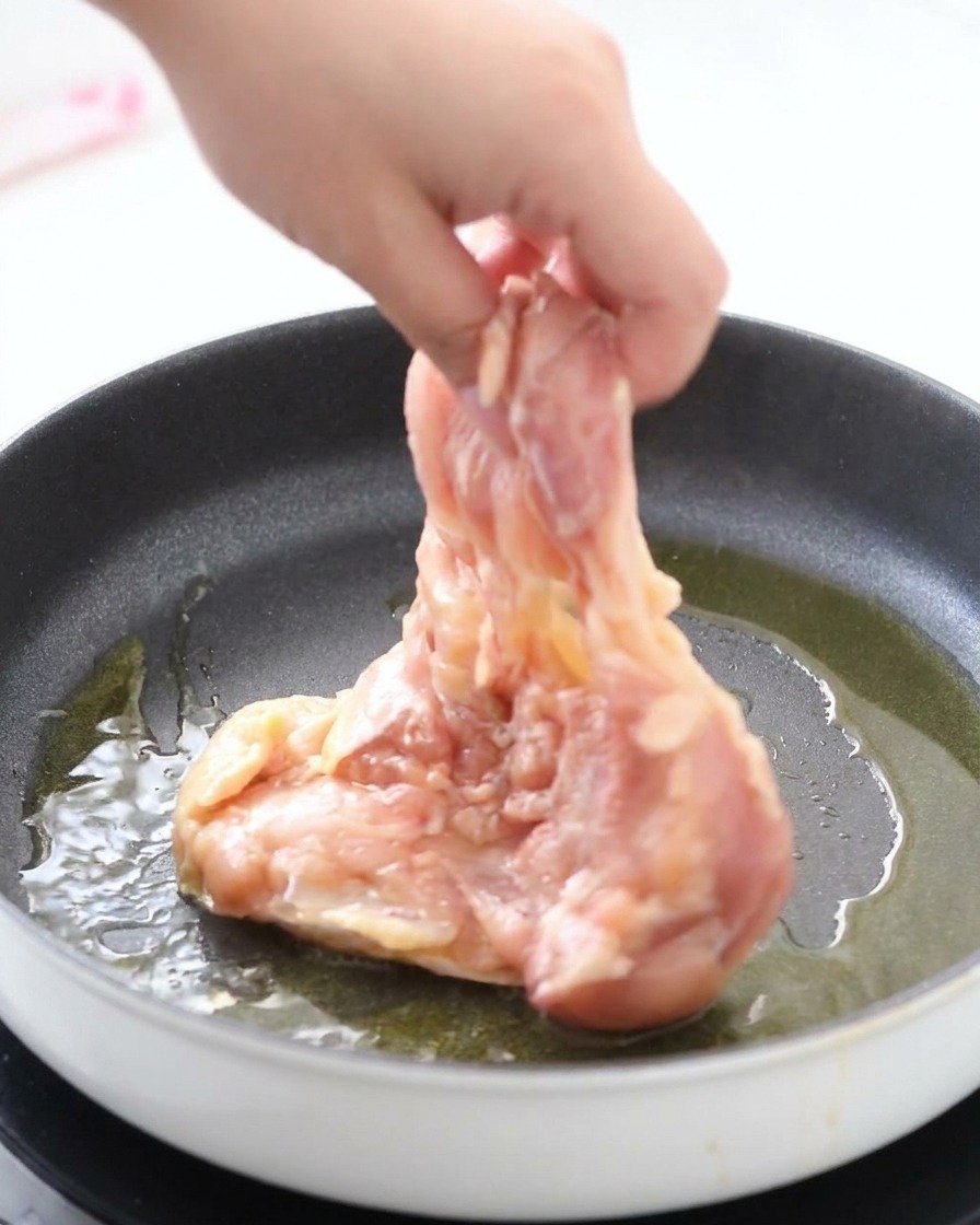 Dépôt dune cuisse de poulet marinée côté peau dans une poêle chaude avec de lhuile brillante.