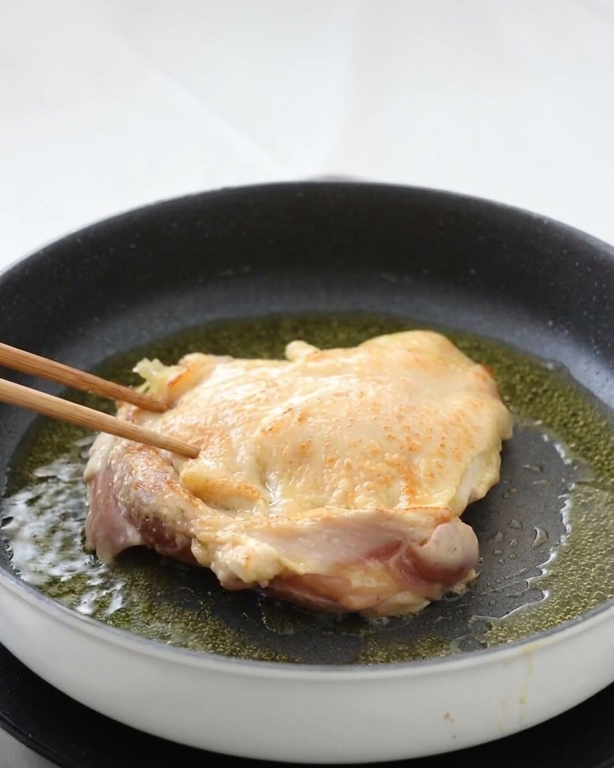 Retournement dune cuisse de poulet avec des baguettes révélant une peau parfaitement croustillante.