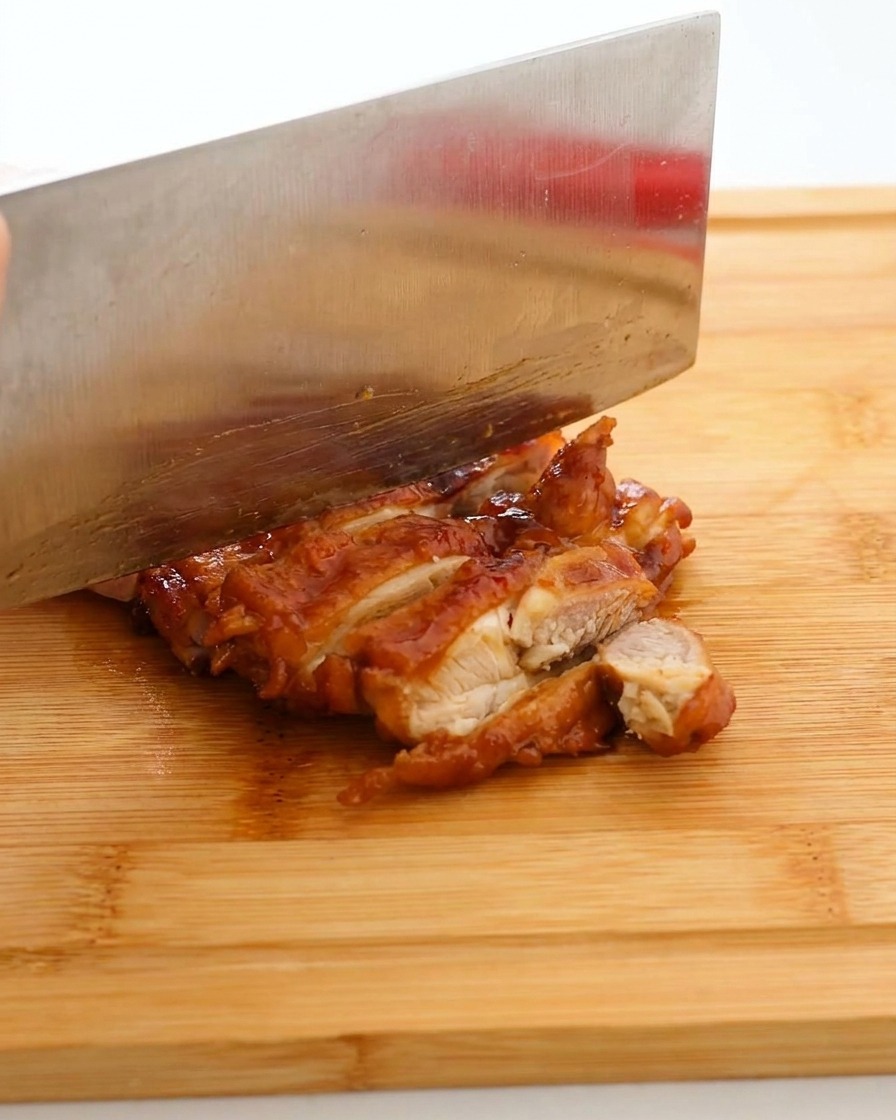 Couteau de cuisine tranchant découpant le poulet laqué en lanières sur une planche en bois.