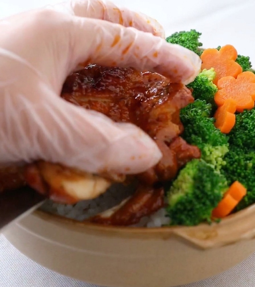 Main disposant soigneusement des brocolis et des fleurs de carottes dans un bol de riz au poulet.