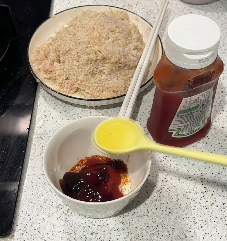 Une cuillère jaune versant de lhuile chaude dans un bol contenant du ketchup et des épices.