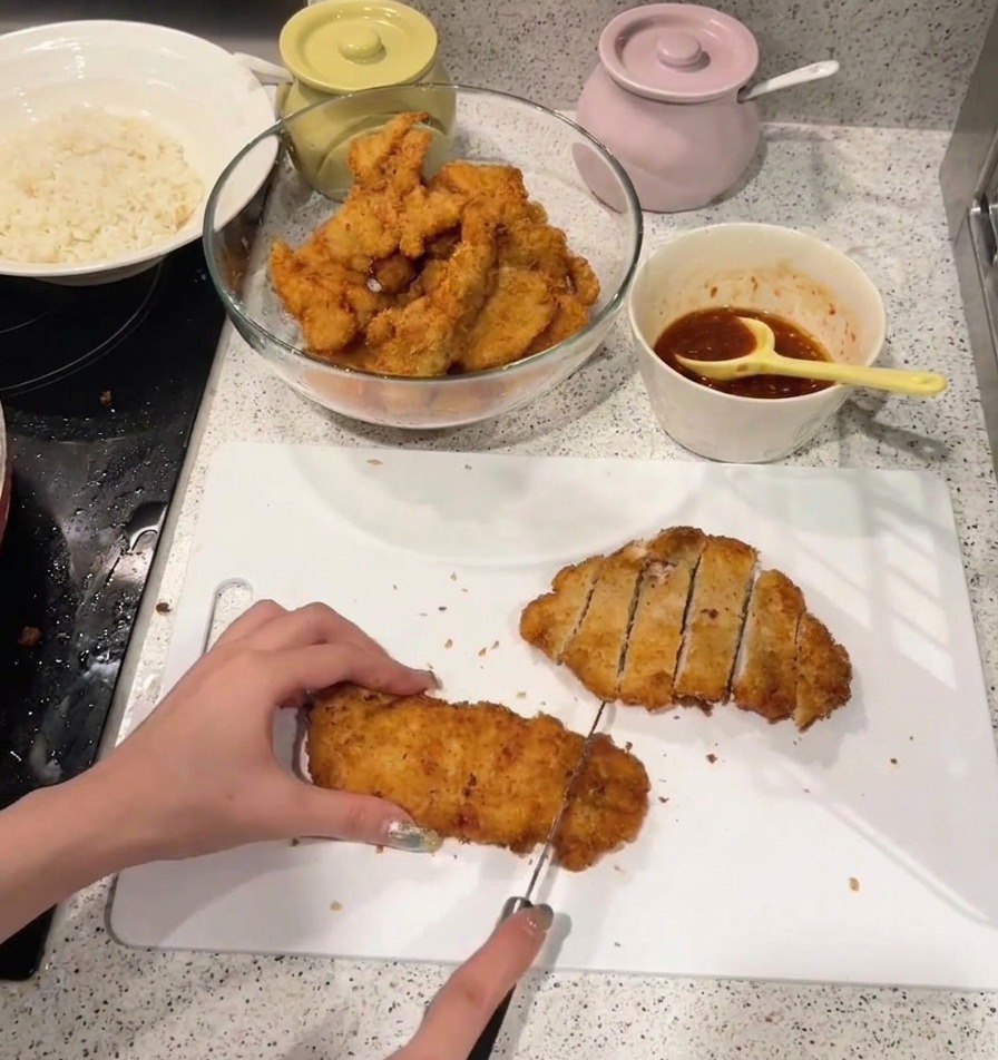 Une personne découpant une escalope de poulet frit dorée en lanières sur une planche à découper blanche.