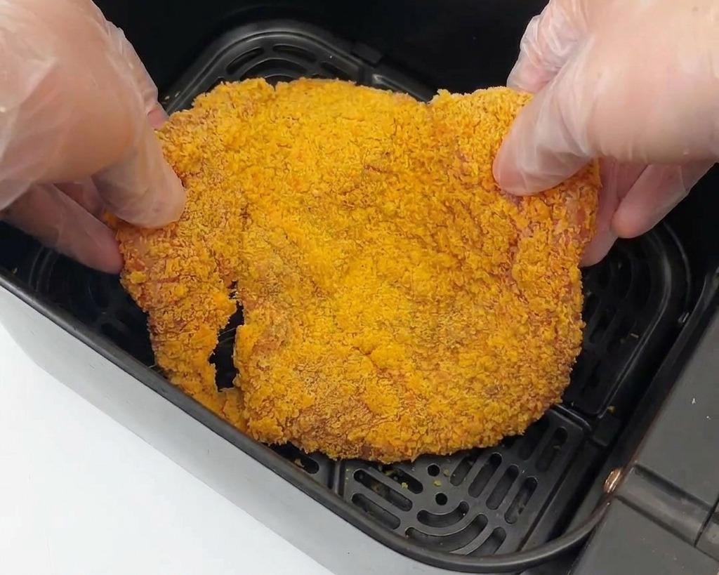 Une main déposant le poulet pané dans le panier dune friteuse à air.