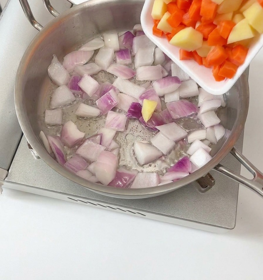 Dés de pommes de terre et de carottes ajoutés à loignon dans la poêle.