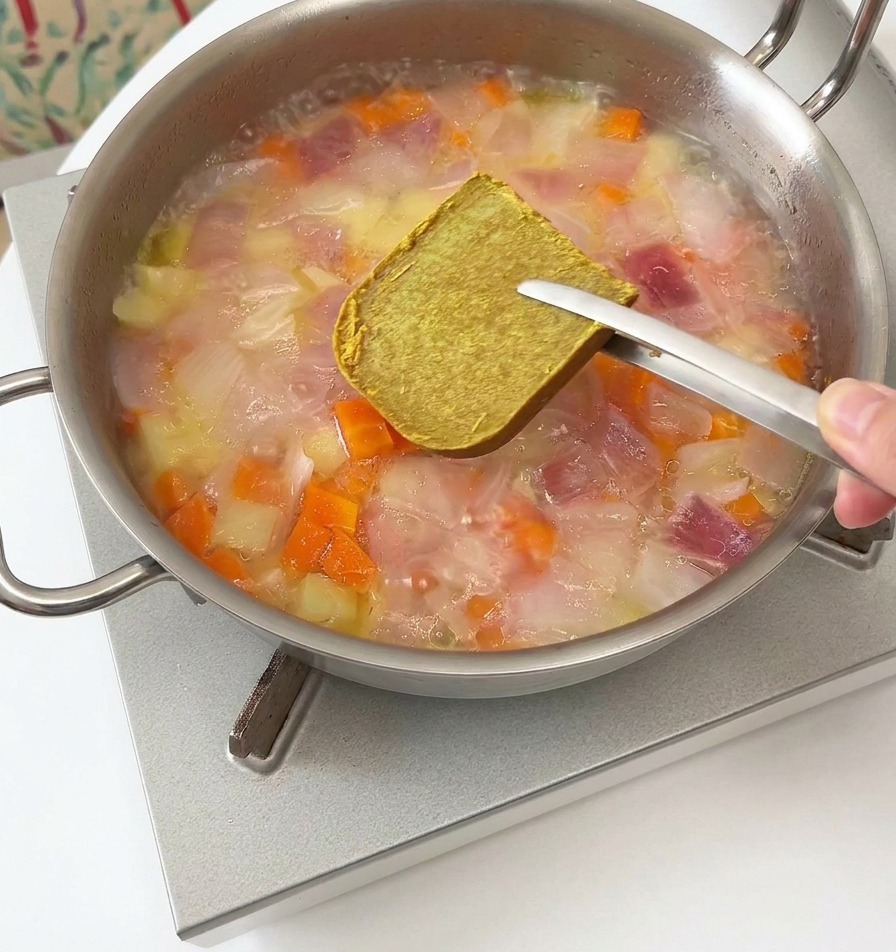 Un cube de roux de curry brun maintenu au-dessus de la poêle fumante.