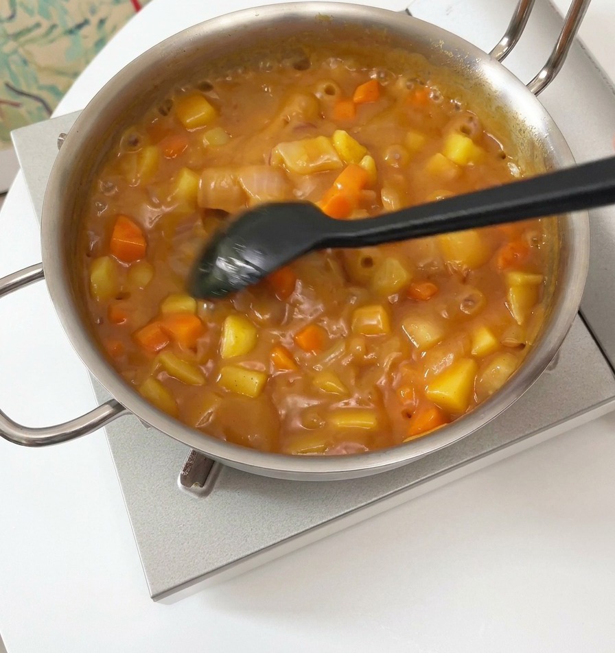 Spatule mélangeant une sauce curry brune et épaisse avec des légumes dans une casserole.