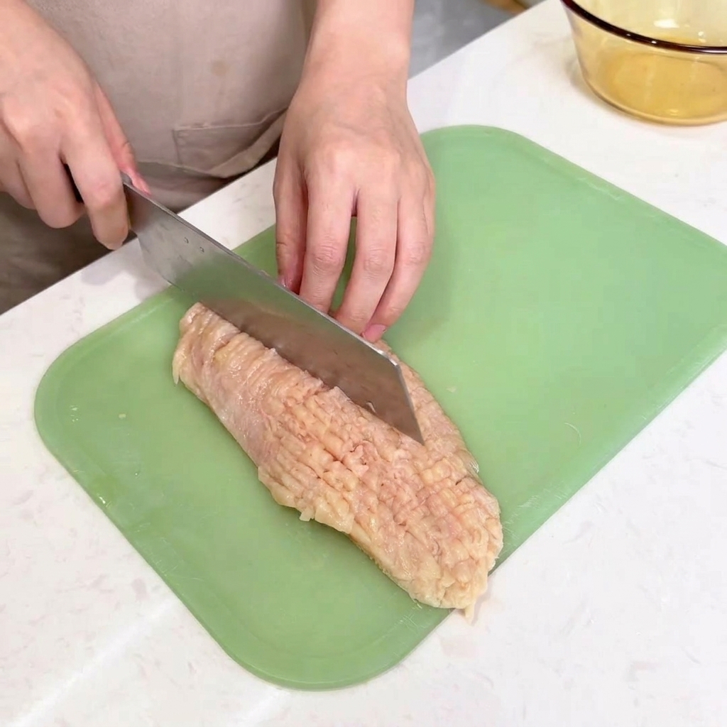 Le dos dun large couteau de chef frappant un blanc de poulet à plat sur une planche à découper pour lattendrir.