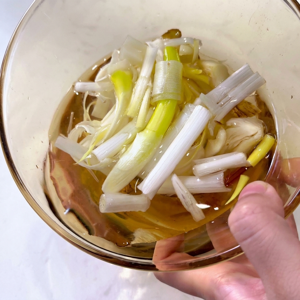 Gros plan dun bol en verre rempli deau avec des morceaux de ciboule et des tranches de gingembre.