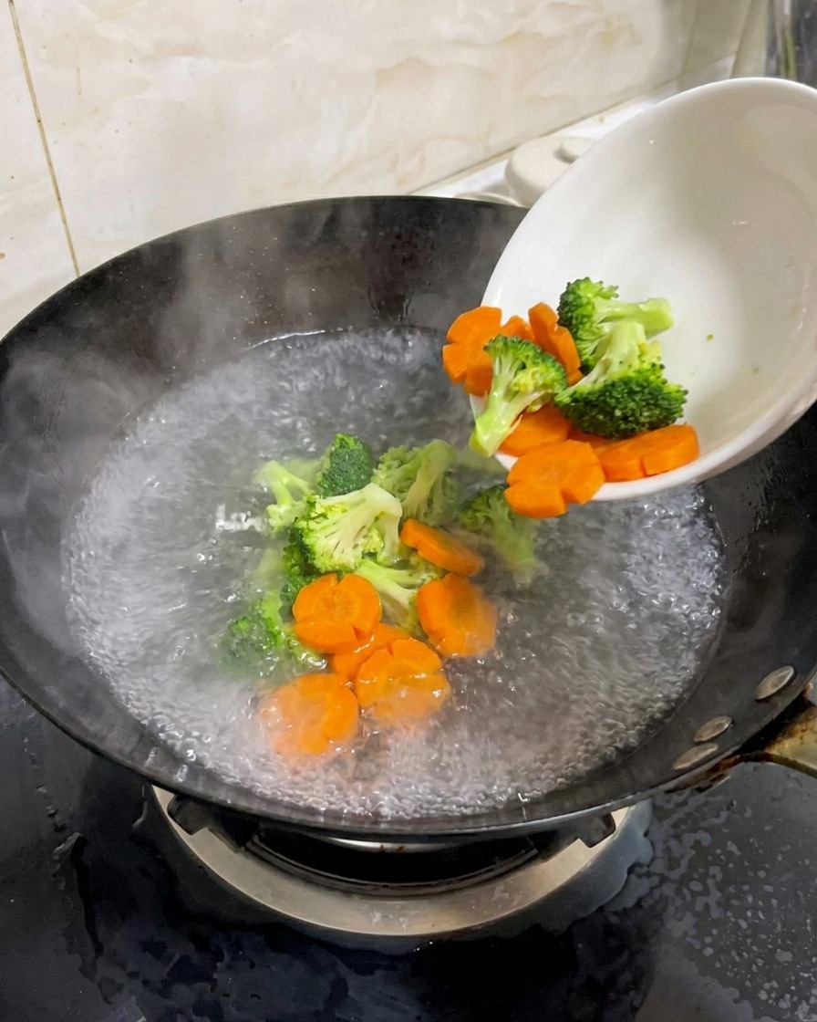 Bouquets de brocoli et carottes en fleurs versés dans un wok deau bouillante salée.