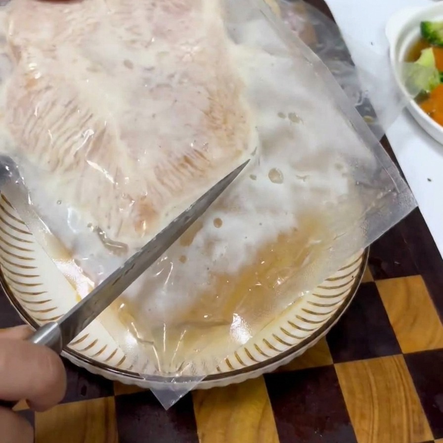 Main ouvrant délicatement un sachet sous vide contenant du poulet mariné avec un couteau de cuisine.