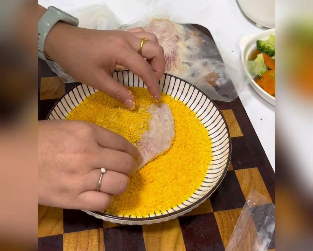 Mains pressant fermement un blanc de poulet mariné dans un bol rempli de chapelure jaune dorée.