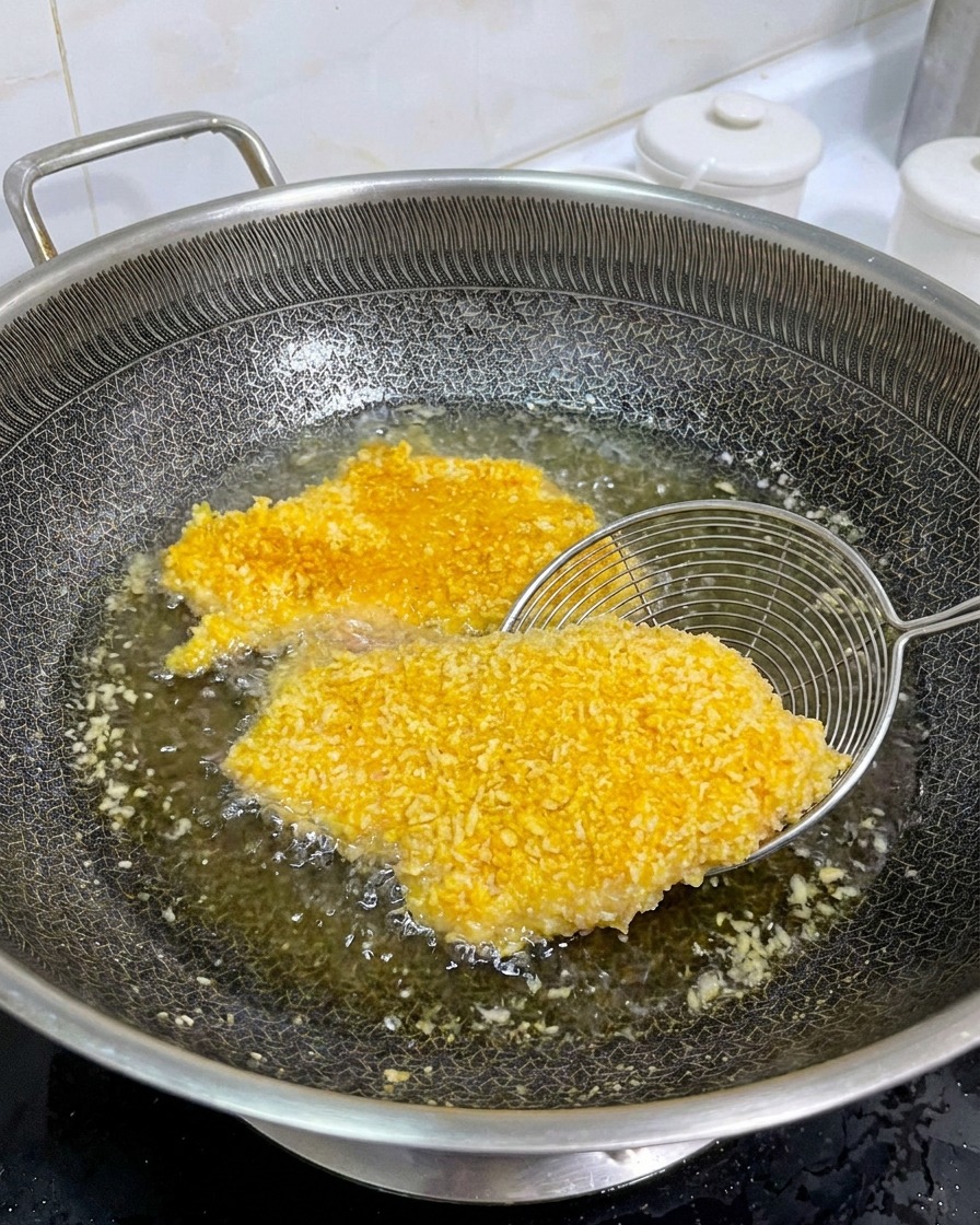 Écumoire métallique soulevant une escalope de poulet katsu parfaitement dorée pour vérifier la cuisson.