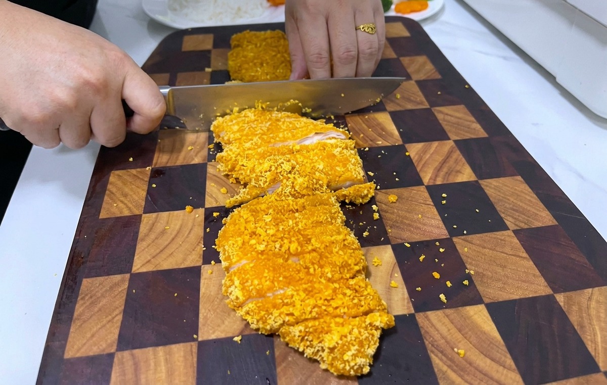 Couteau de chef tranchant une escalope de poulet katsu croustillante sur une planche à découper en bois.