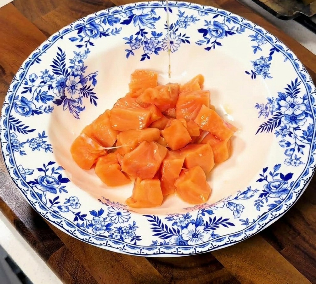 Filet de marinade liquide versé sur des cubes de saumon cru dans un bol en céramique aux motifs floraux.