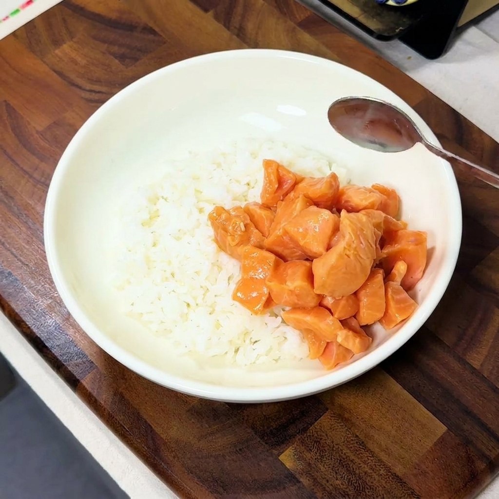 Cubes de saumon mariné déposés à la cuillère sur un côté dun bol rempli de riz blanc fumant.