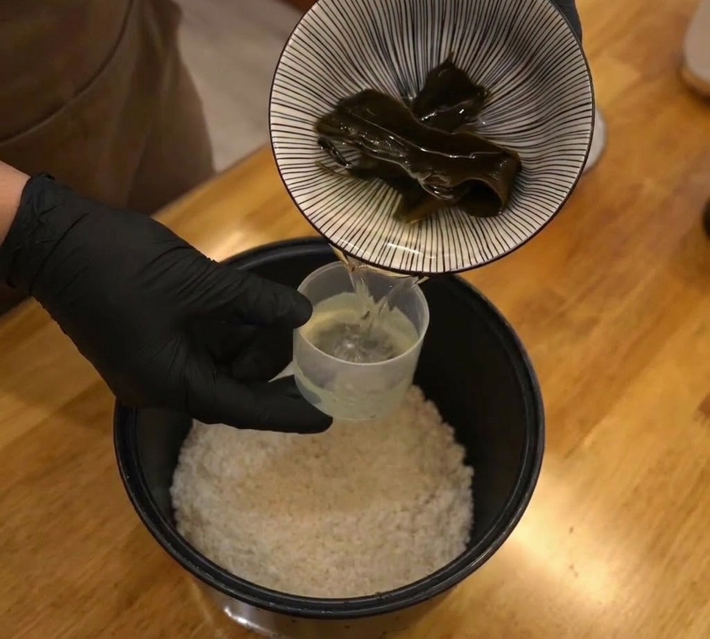 Un morceau de kombu séché placé dans la cuve dun cuiseur à riz avec le riz blanc et leau.