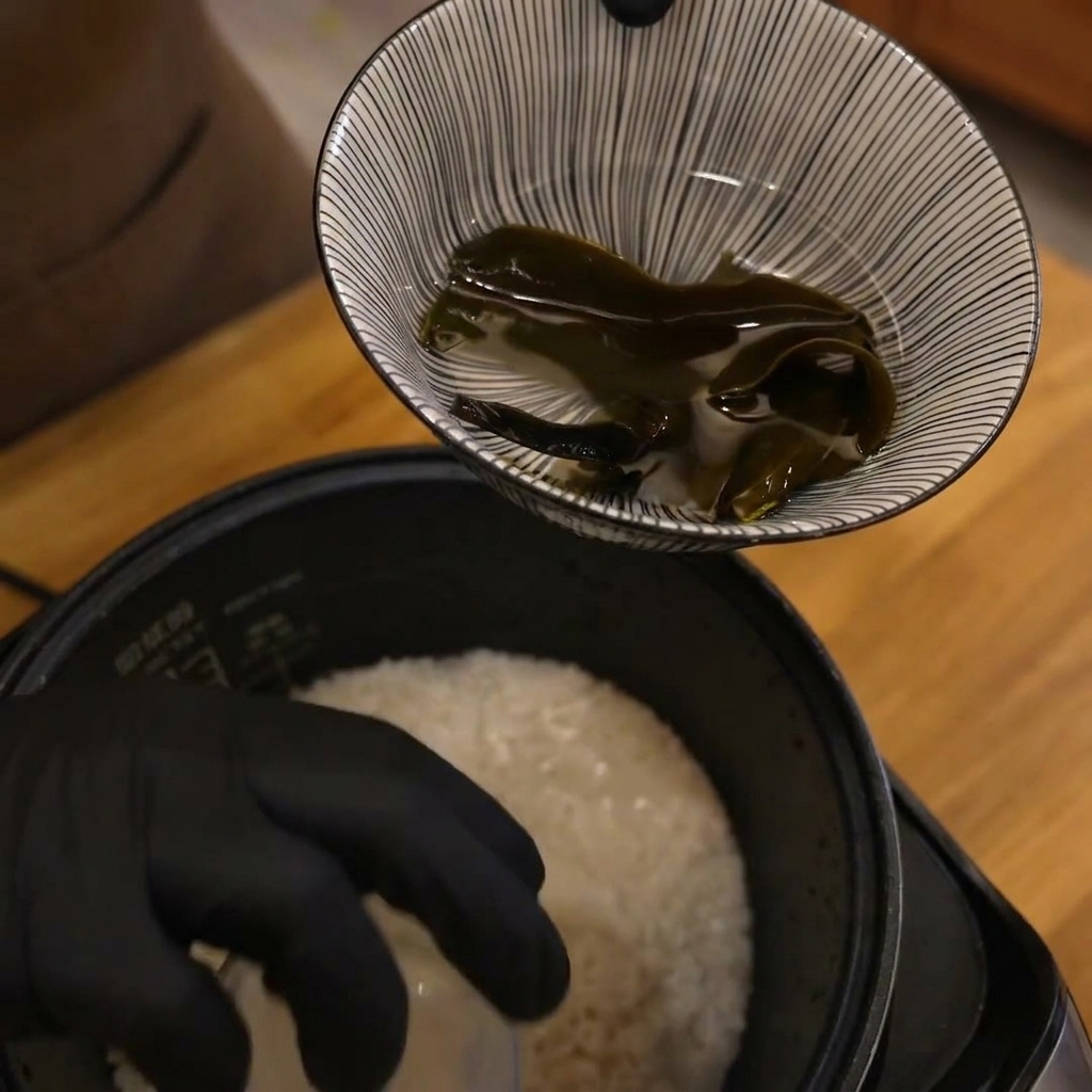 Une main tenant un verre doseur au-dessus dune cuve de riz blanc avant la cuisson.