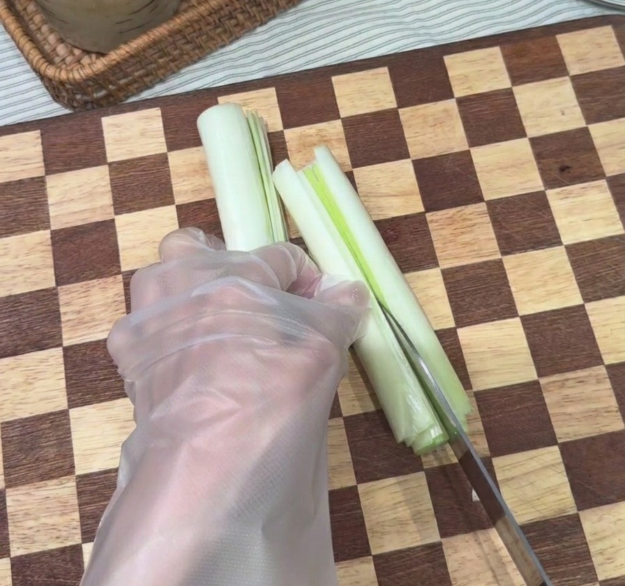 Main utilisant un couteau de chef pour émincer une tige de ciboule en fines lanières sur une planche à découper.