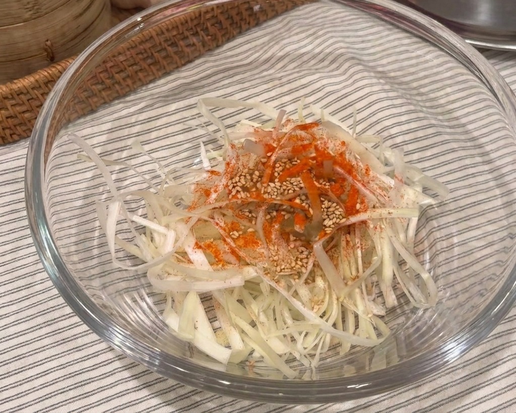 Bol en verre contenant de la ciboule émincée, surmontée dun petit tas de poudre de piment rouge et de sésame blanc.