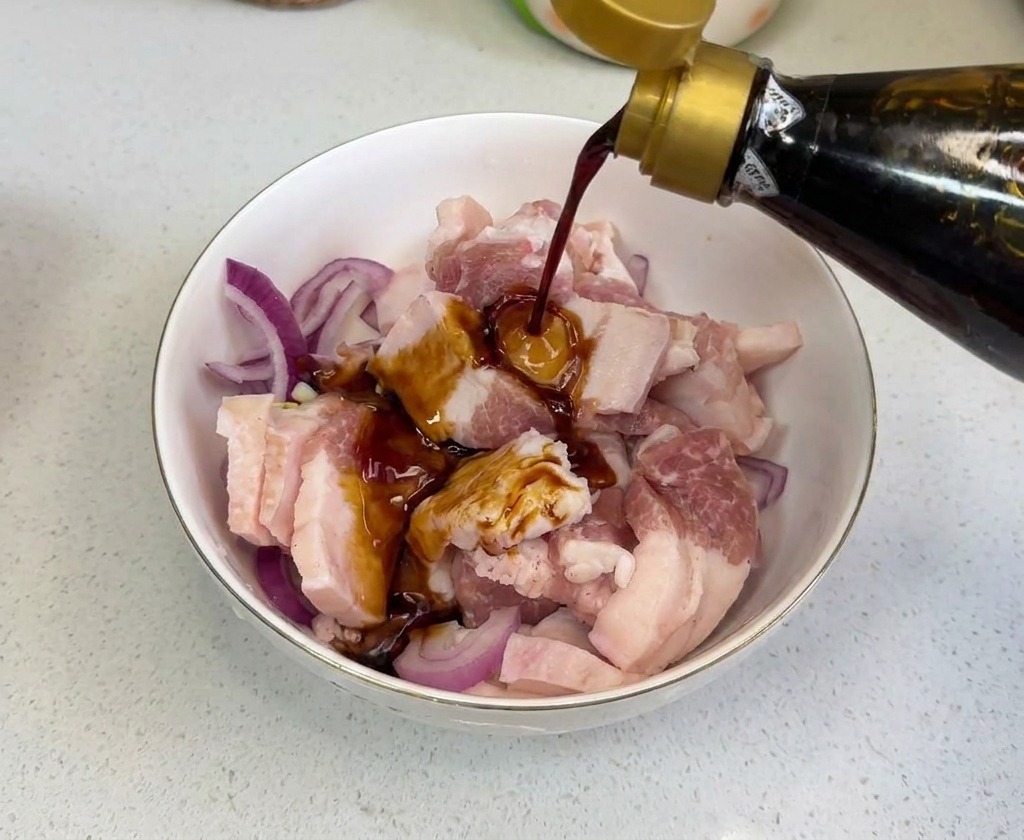 De la sauce soja foncée versée dune bouteille en verre sur de la viande crue et des oignons tranchés.
