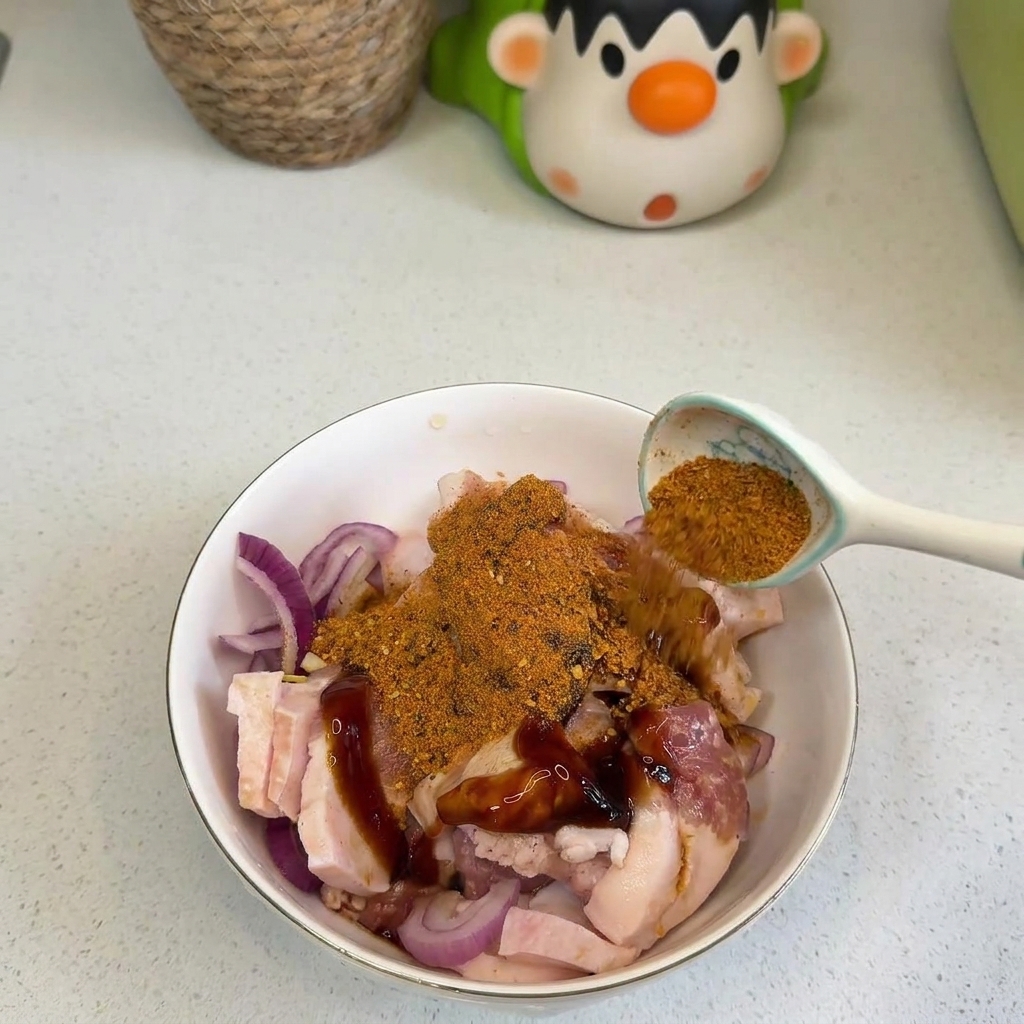 Une main versant une cuillerée dépices BBQ orange et de piment rouge sur la poitrine de porc et les oignons.