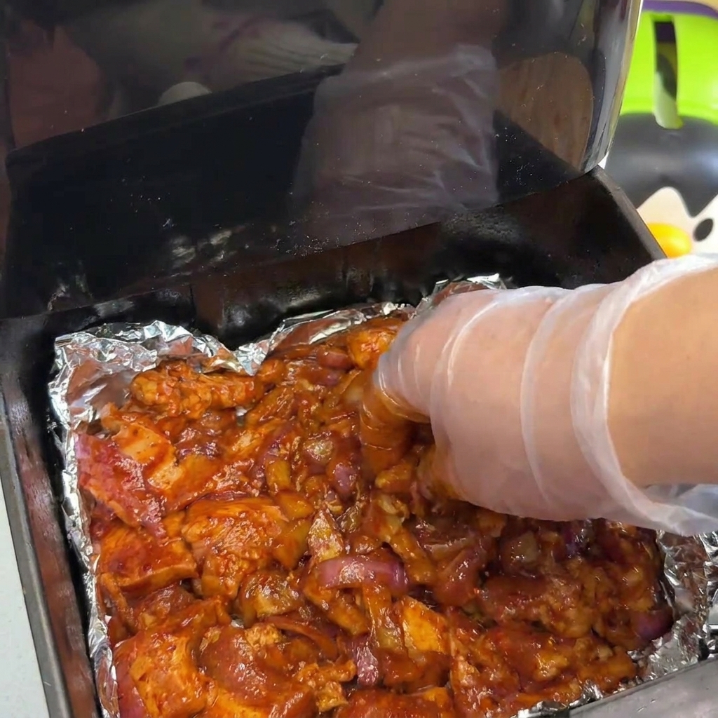 Une main étalant une couche épaisse de porc mariné et doignons dans le panier de la friteuse.
