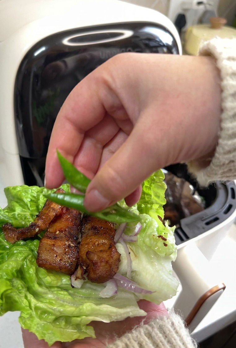 Une main déposant deux tranches de piment vert sur un wrap de laitue garni de porc et doignons.