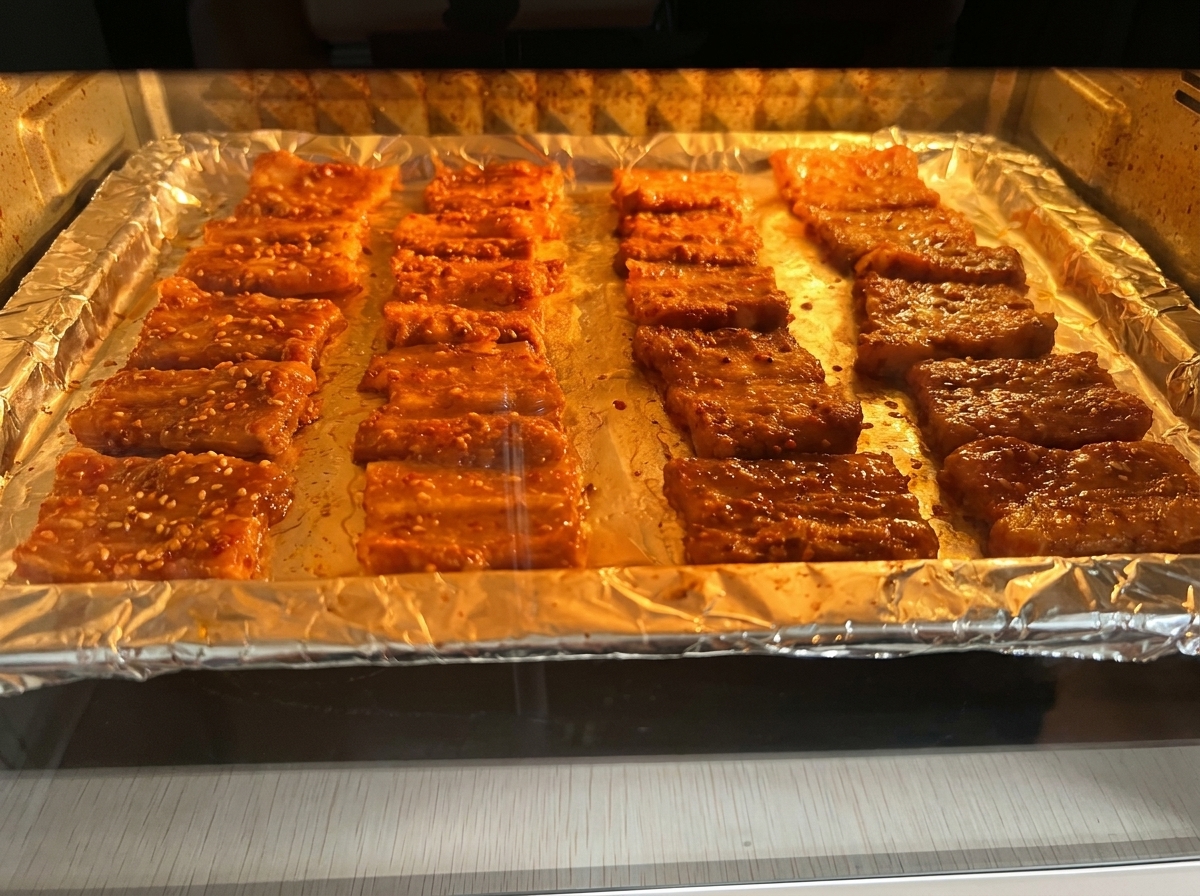 Tranches de porc marinées en train de rôtir sur une plaque recouverte daluminium dans un four à léclairage chaleureux.