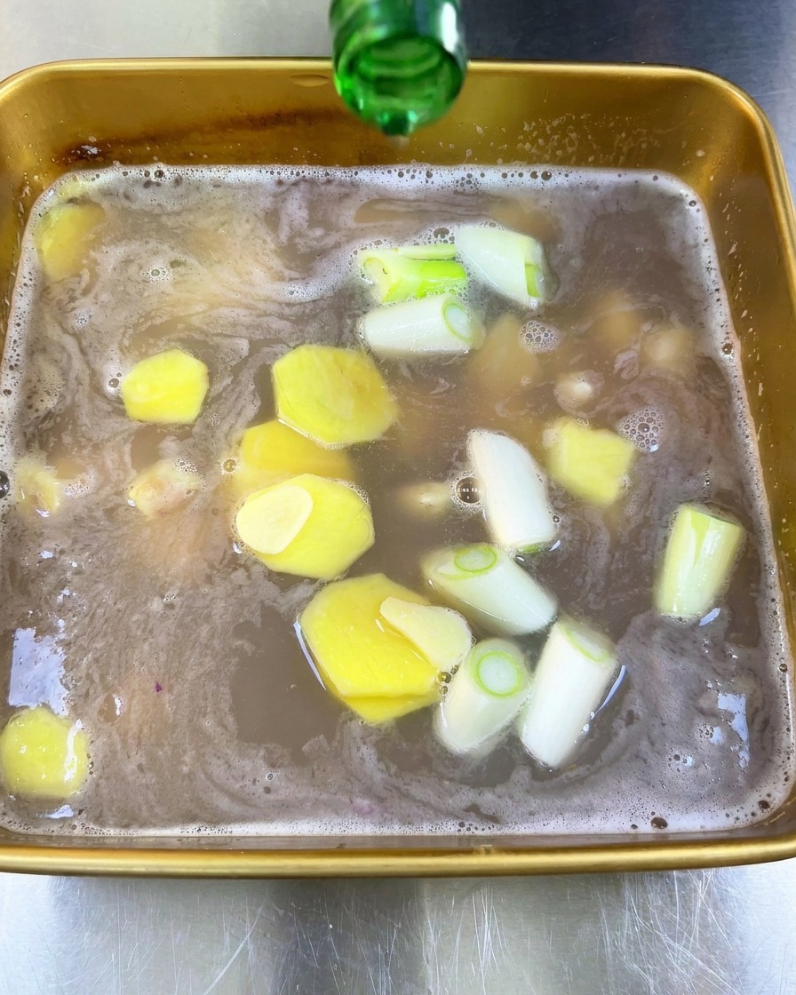 Du vin de riz clair versé depuis une bouteille en verre vert dans la marinade contenant les aromates.