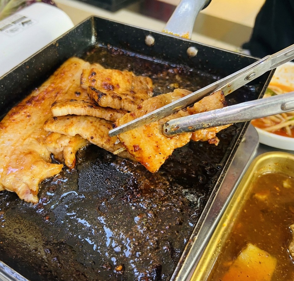 Gros plan de tranches de porc coupées avec des ciseaux de cuisine sur une poêle grill, montrant une belle croûte brune.