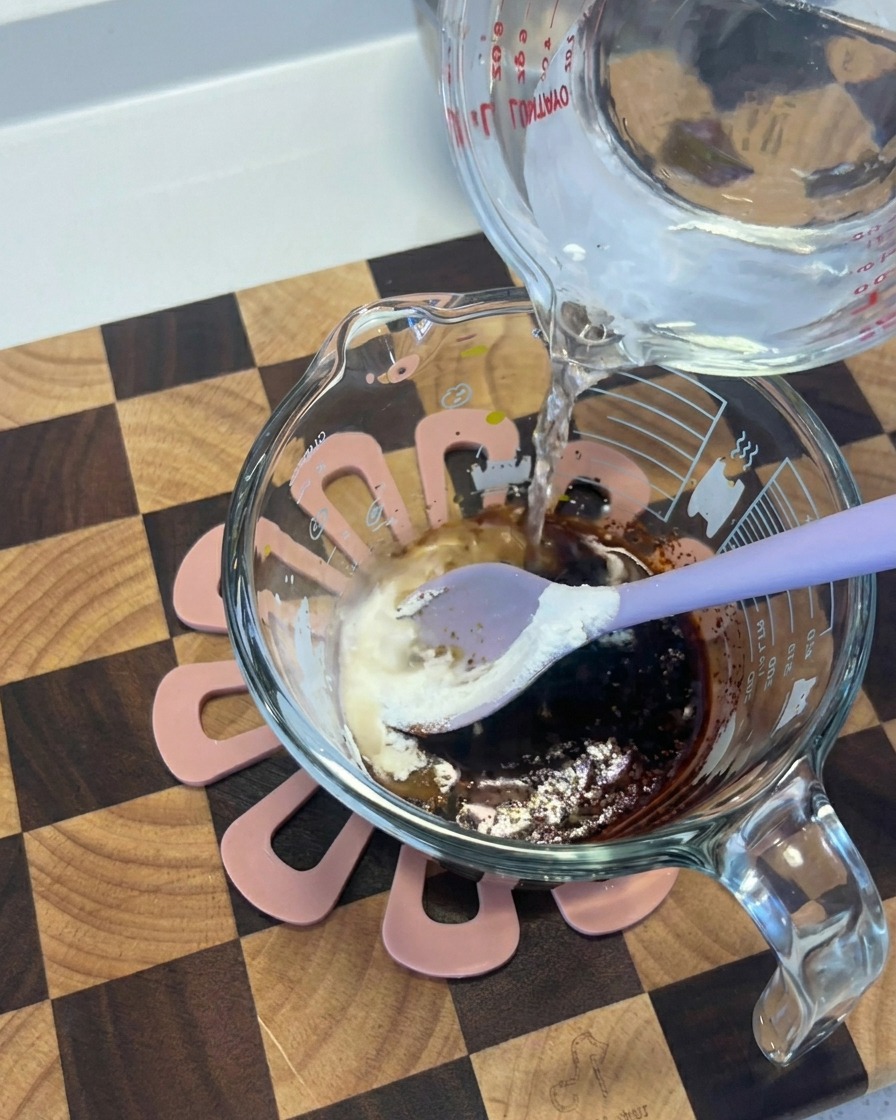 De leau versée dun récipient en verre dans une tasse contenant un mélange sombre de sauce soja et dépices.
