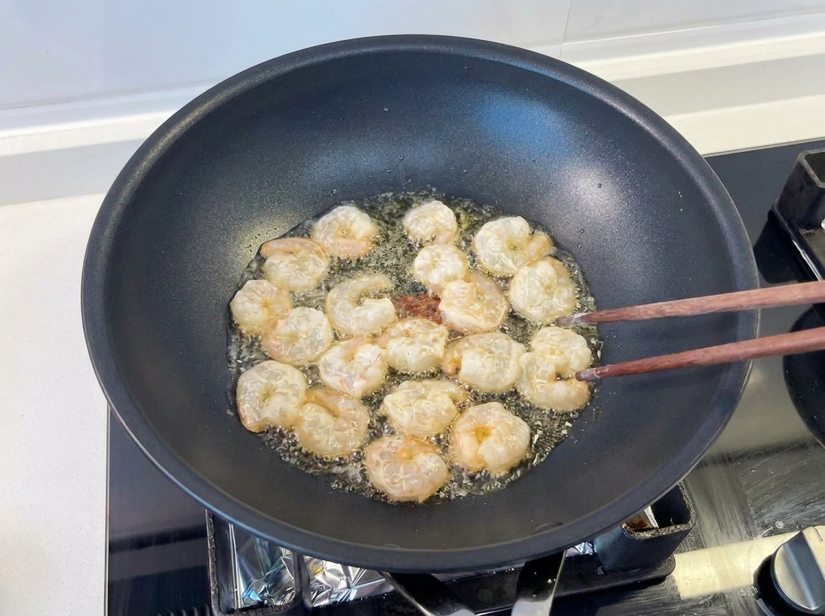 Plusieurs crevettes sautées avec des baguettes en bois dans un wok noir avec de lhuile frémissante.