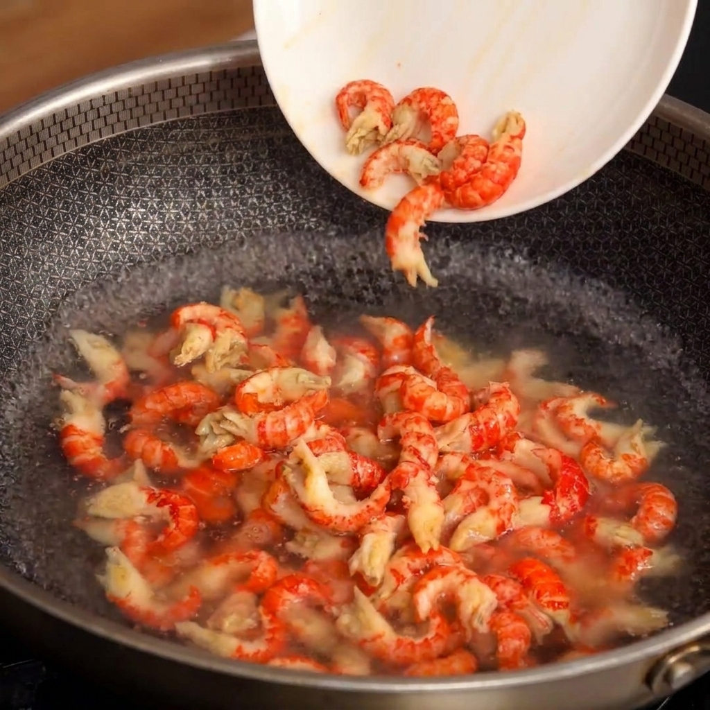 Une assiette versant des queues décrevisses décortiquées dans un wok deau bouillante.